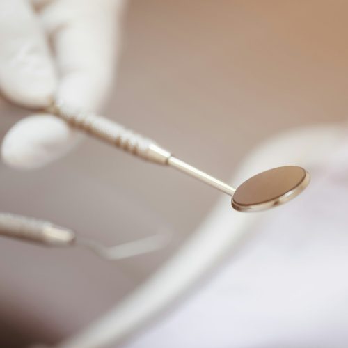 The dentist's hand holds the tooth checker and a mirror for checking and caring for dentist's tools