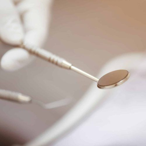 The dentist’s hand holds the tooth checker and a mirror for checking and caring for dentist’s tools The dentist's hand holds the tooth checker and a mirror for checking and caring for dentist's tools